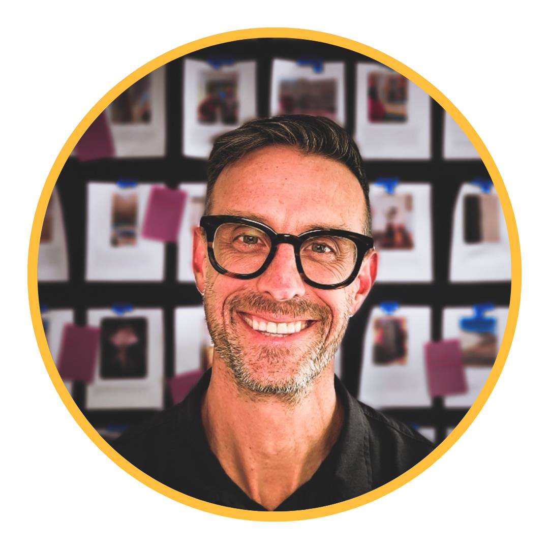 A white man in glasses in front of a wall of images